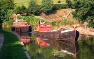 Historic working narrow boats on the Macclesfield Canal in Cheshire, England. The leading boat, Forget Me Not is hauling the un-powered butty Lilith. This became a familiar operating pattern once motors began to replace horses. (Source: Wikipedia. Image is Public Domain)